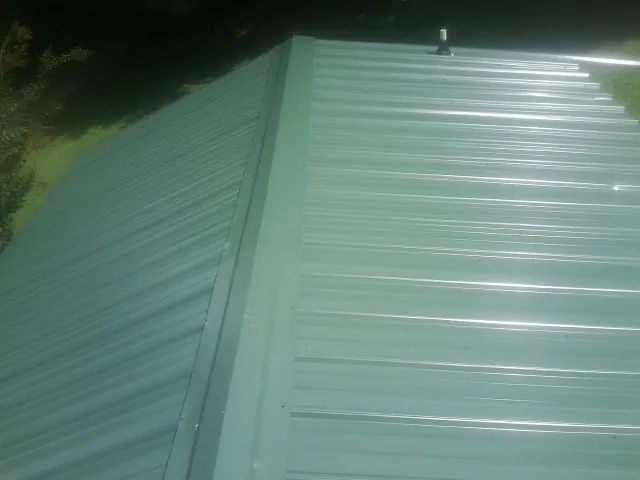 New green metal panels meeting at the ridge of a roof — Flat Roof Repair work by our crew in Medford